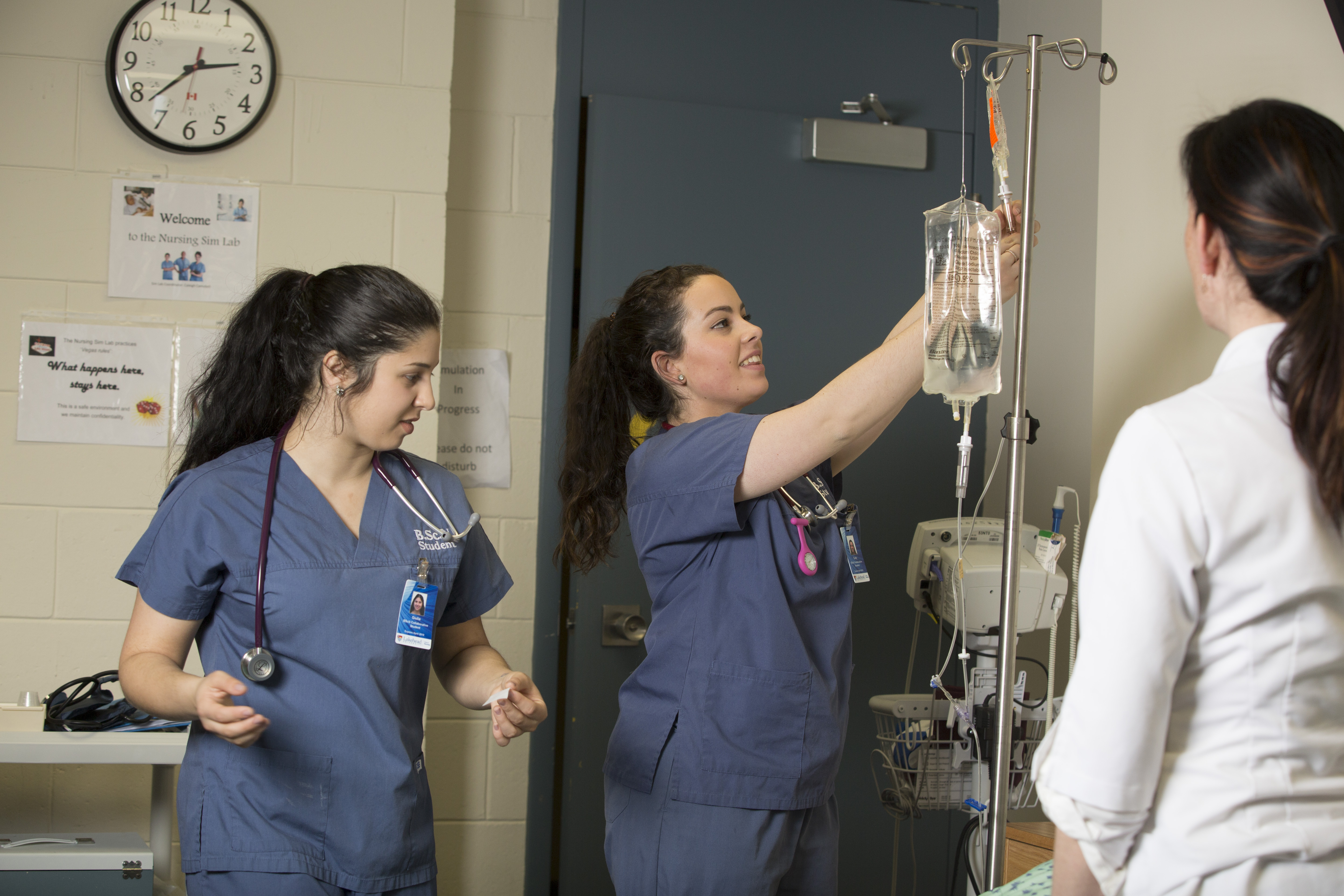 Nursing student adjust IV bag while instructor looks on.