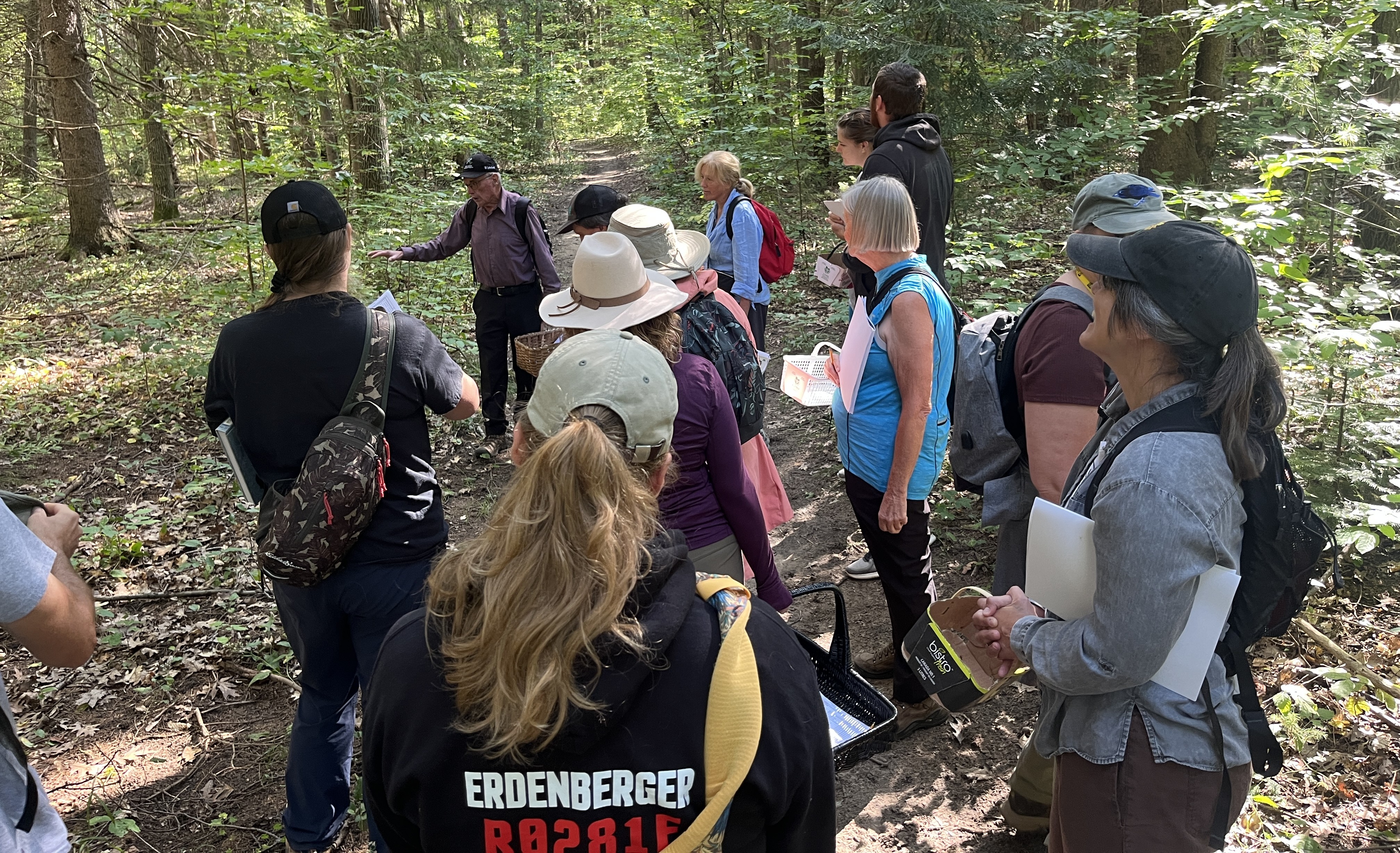 2026 OMNP Mushroom Workshop A group of people in a forest holding baskets listen to an older man speak