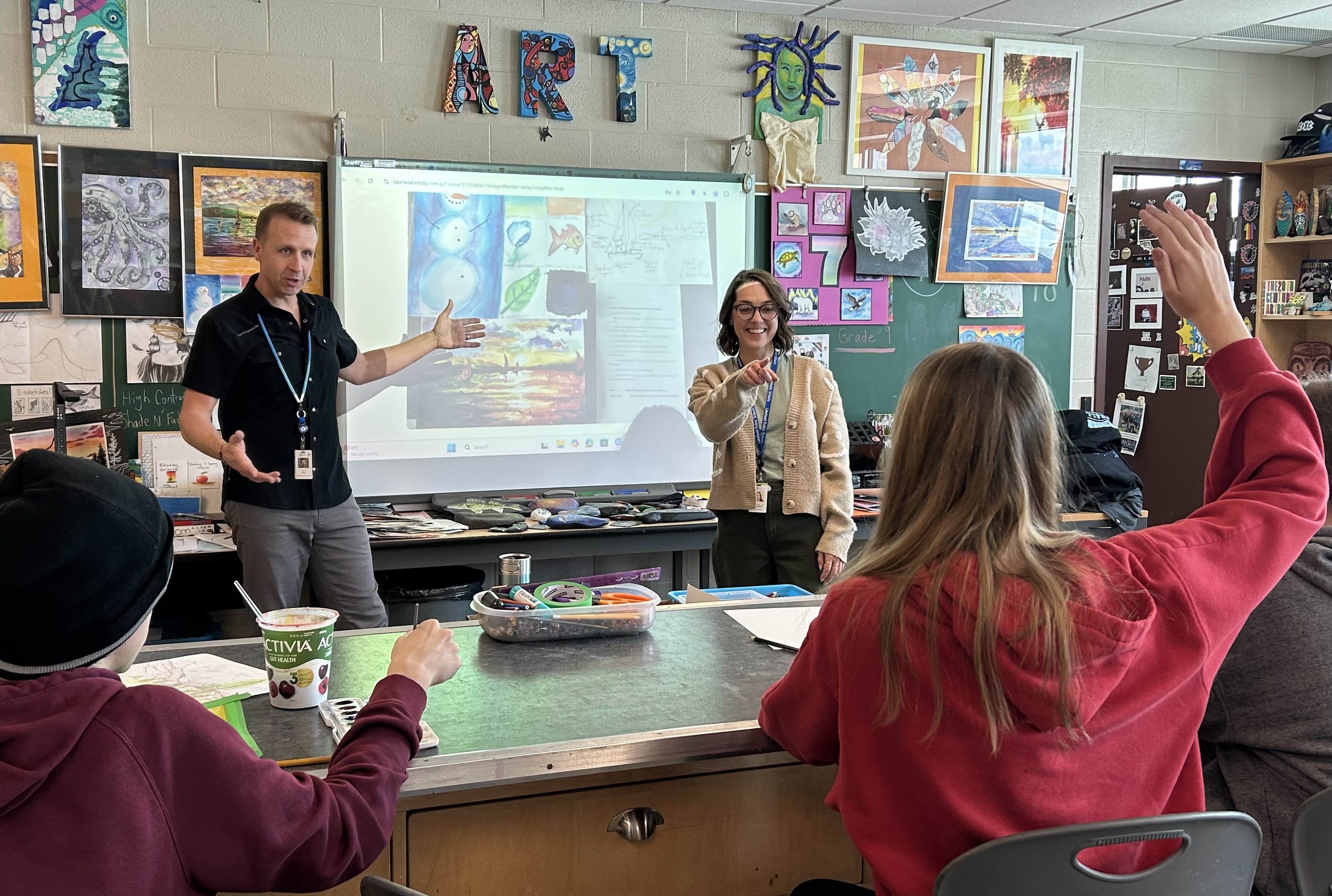 Keith Ailey and Taylor Anderson give a presentation in an art classroom in front of students seated at a desk