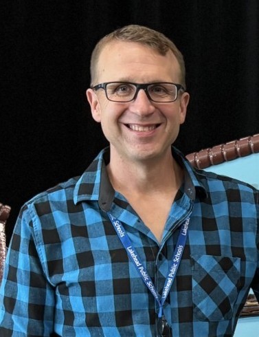 Keith Ailey Headshot Keith Ailey, wearing a checked shirt and glasses, smiles at the camera
