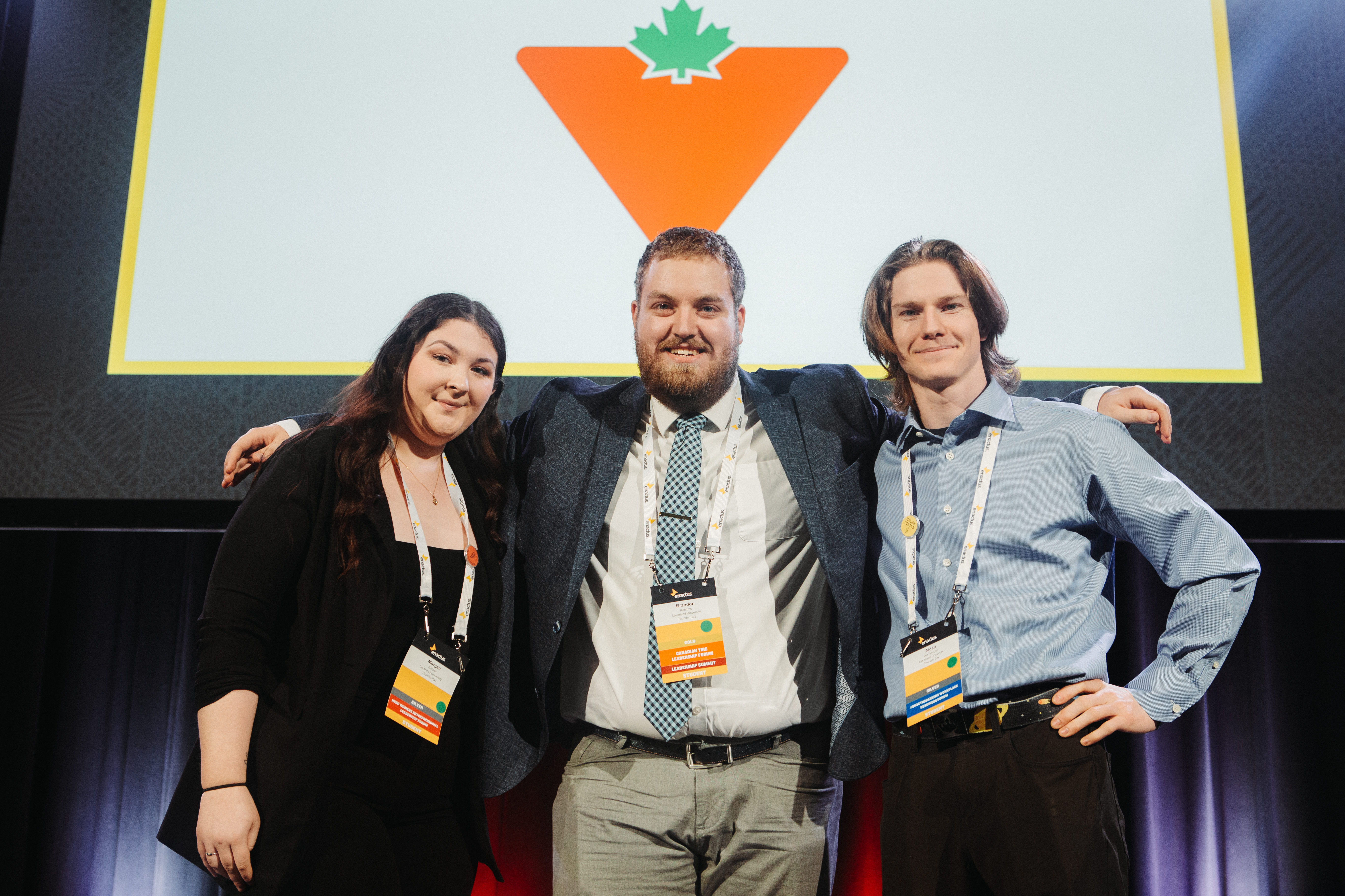 Brandon Rehfuhs stands on stage with his arms around teammates Morgan Gordon and Aidan Woodhouse at the 2024 Enactus Competition 