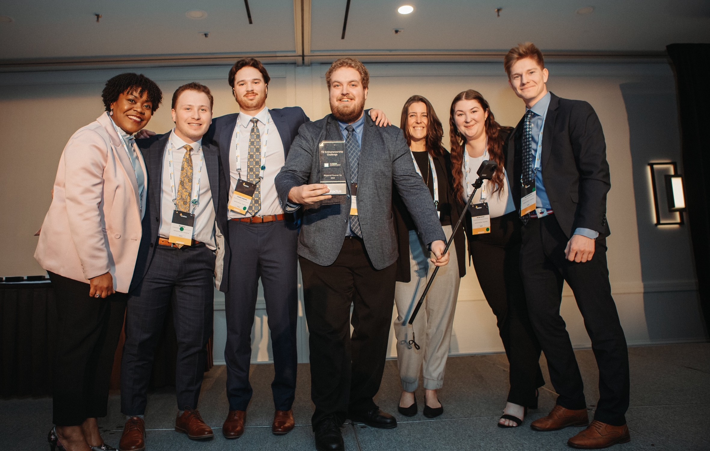 Brandon Rehfuhs holds a 2024 Enactus TD Entrepreneurship Challenge Regional Runner Up Award while standing with his teammates and officials
