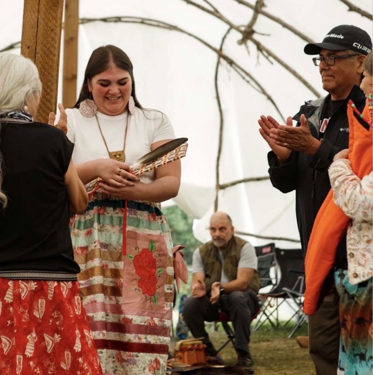 Céline Wick holds an eagle feather while surrounded by people who are clapping