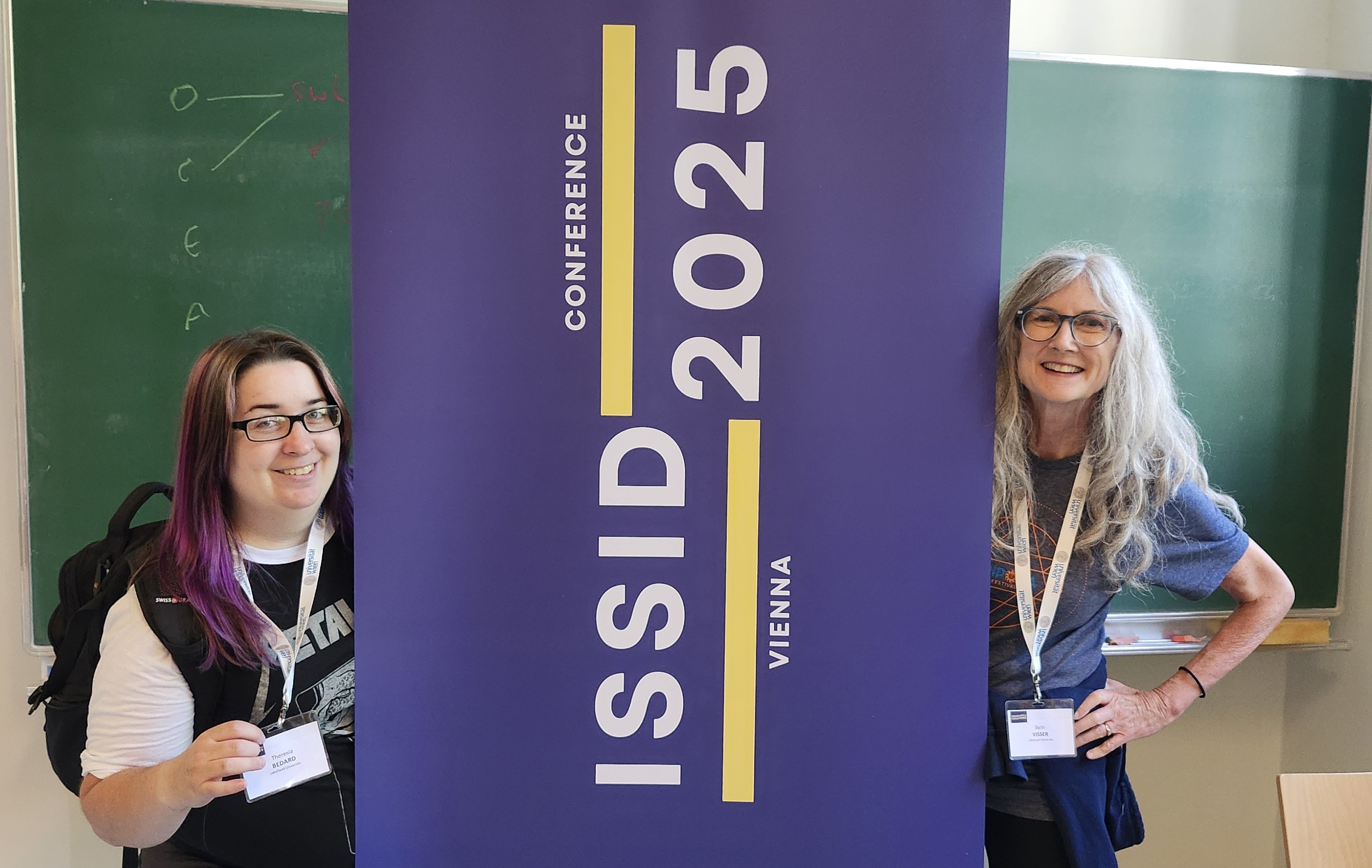 Theresia Bedard and Dr. Beth Visser stand on either side of an ISSID 2025 Conference banner