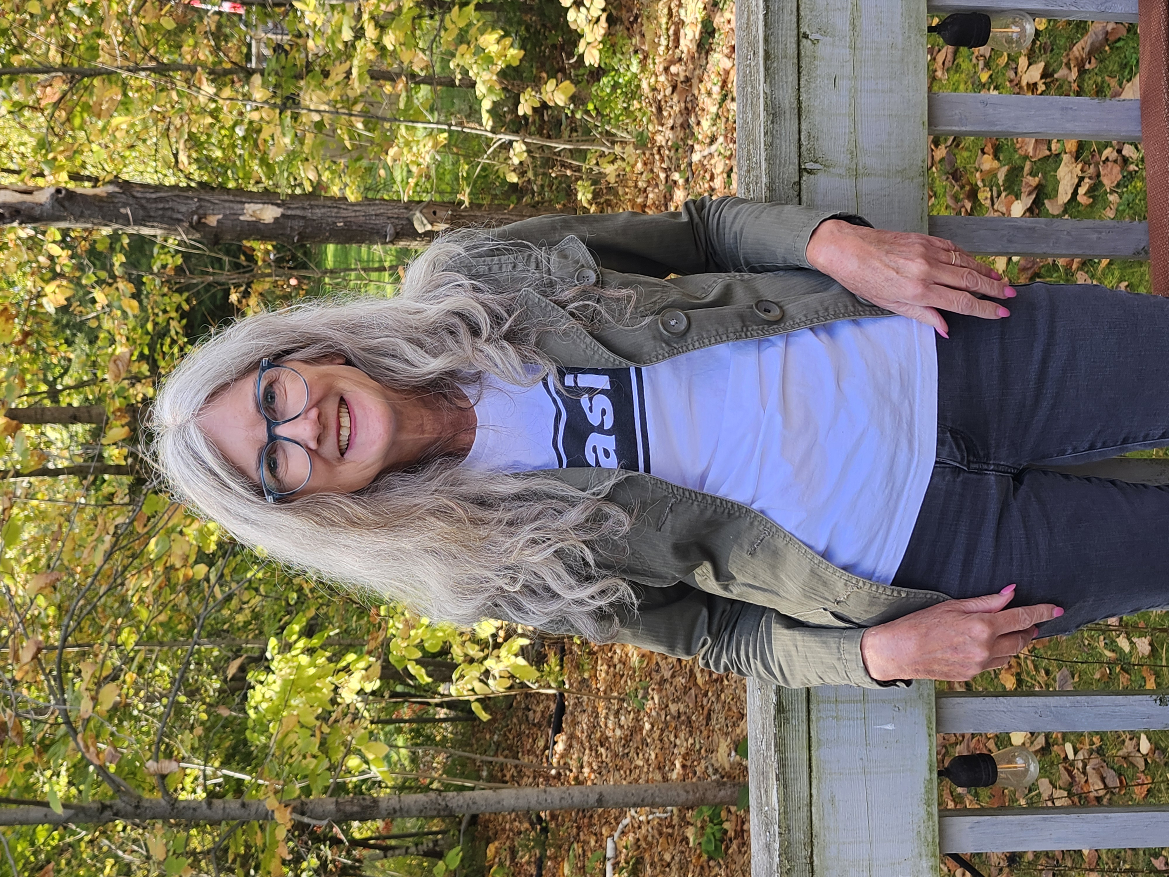 Dr. Beth Visser leans against a wooden deck railing in a yard with trees and fallen leaves