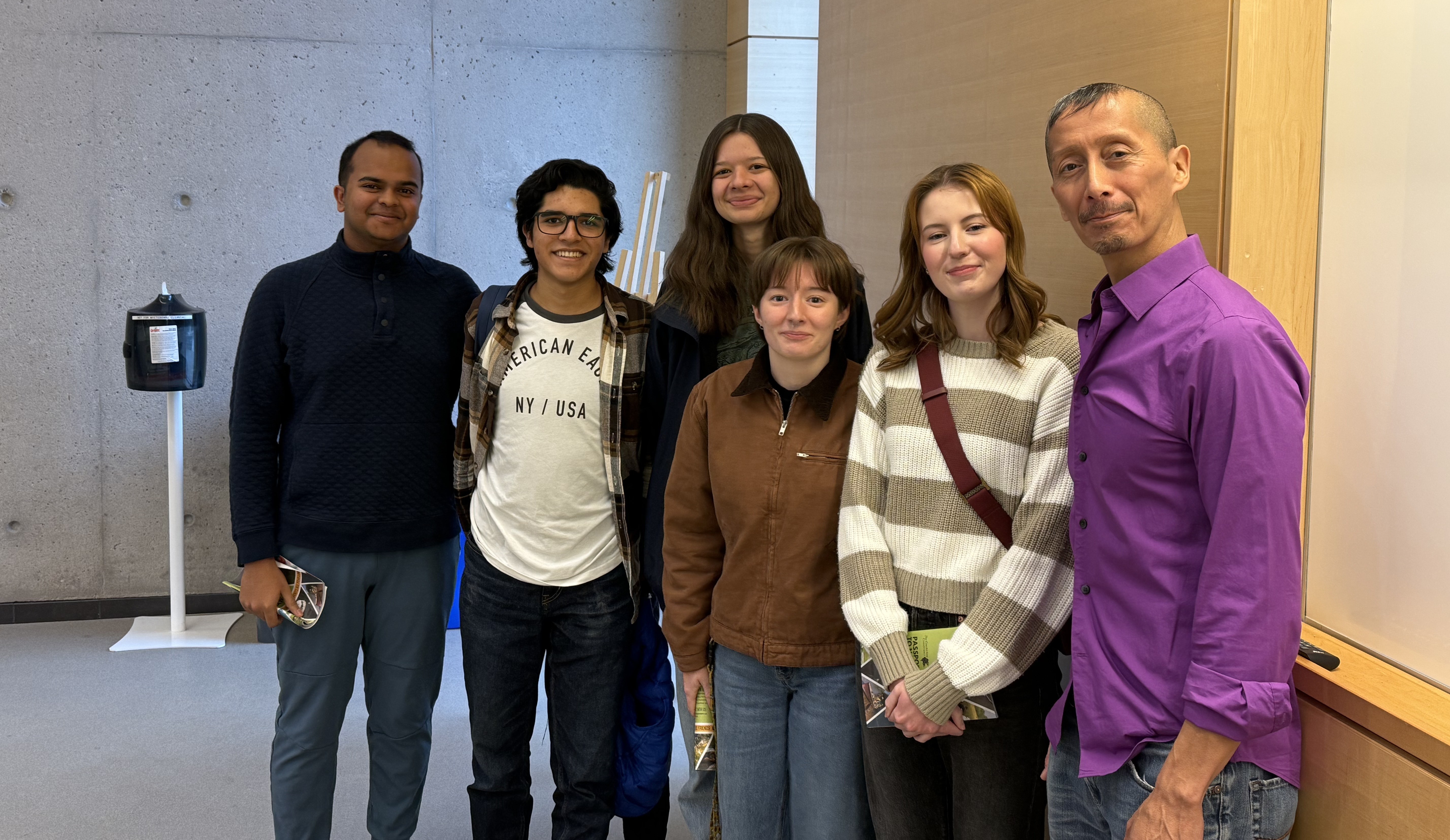 A group of six people, including Dr. Gerardo Reyes, stand beside each other in a building with concrete walls and wooden panelling
