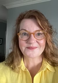 A head-and-shoulders image of a woman wearing a yellow shirt and glasses