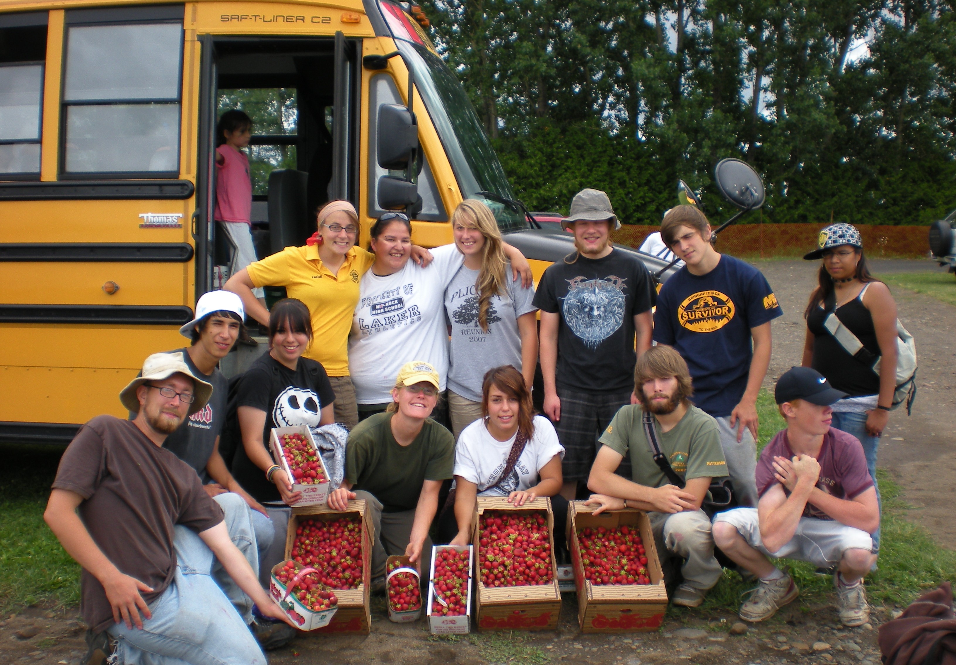Erin Beagle, students, and staff pose in front of a yellow school bus while displaying baskets and boxes of strawberries 