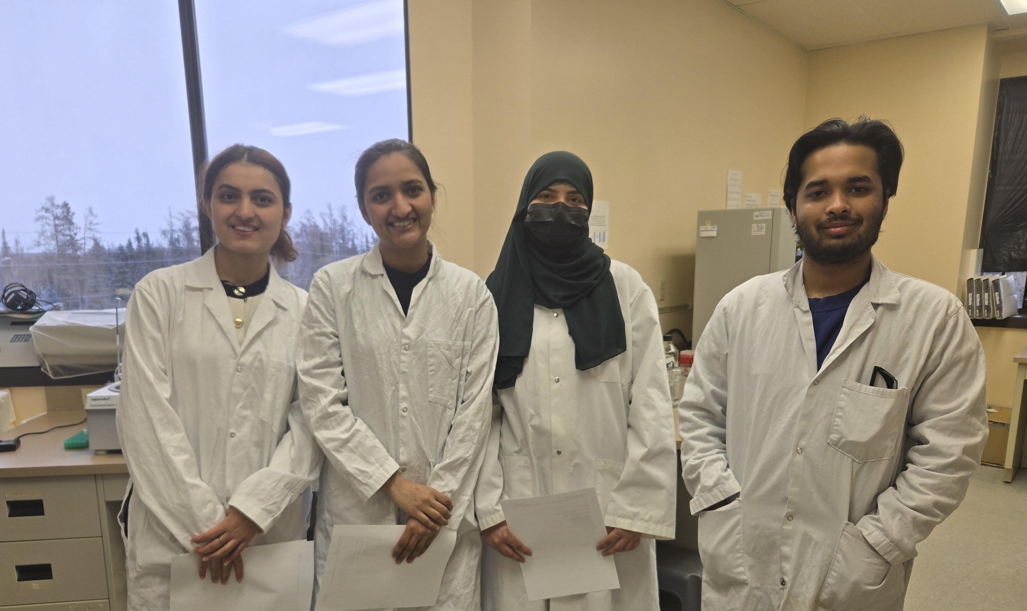 Faiz Mahmud and three young women, all wearing white lab coats, stand in a laboratory space