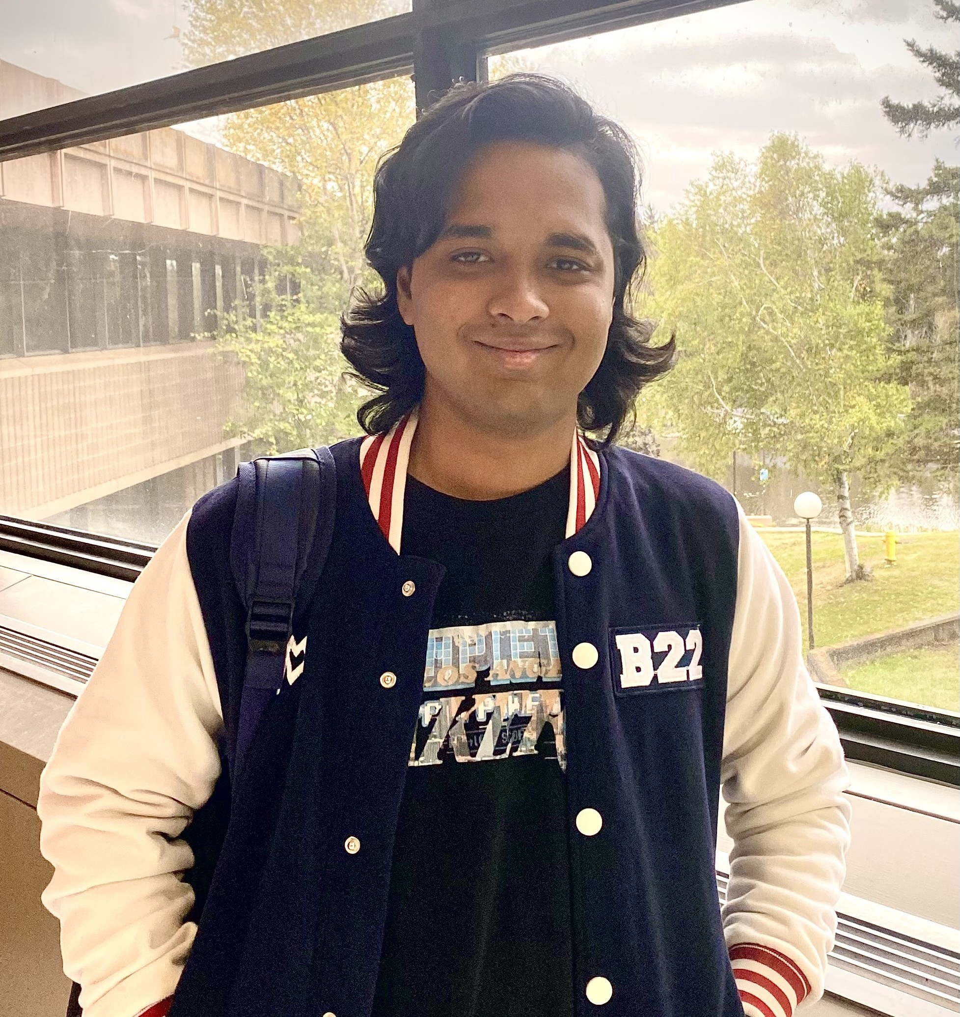 Faiz Mahmud stands in front of a window in the Centennial Building that overlooks trees and Lake Tamblyn