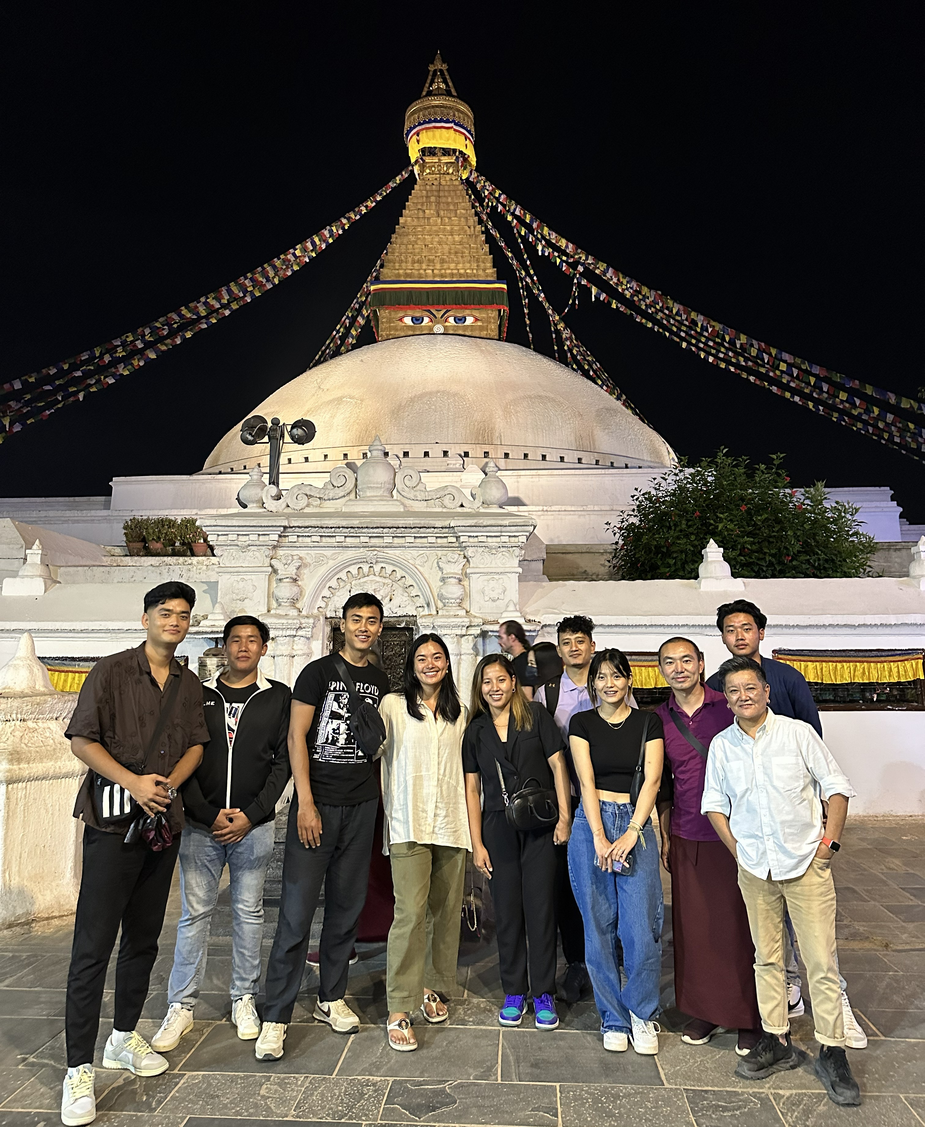 Jigme Tsering and a group of people stand in front of the Boudhanath Stupa at night