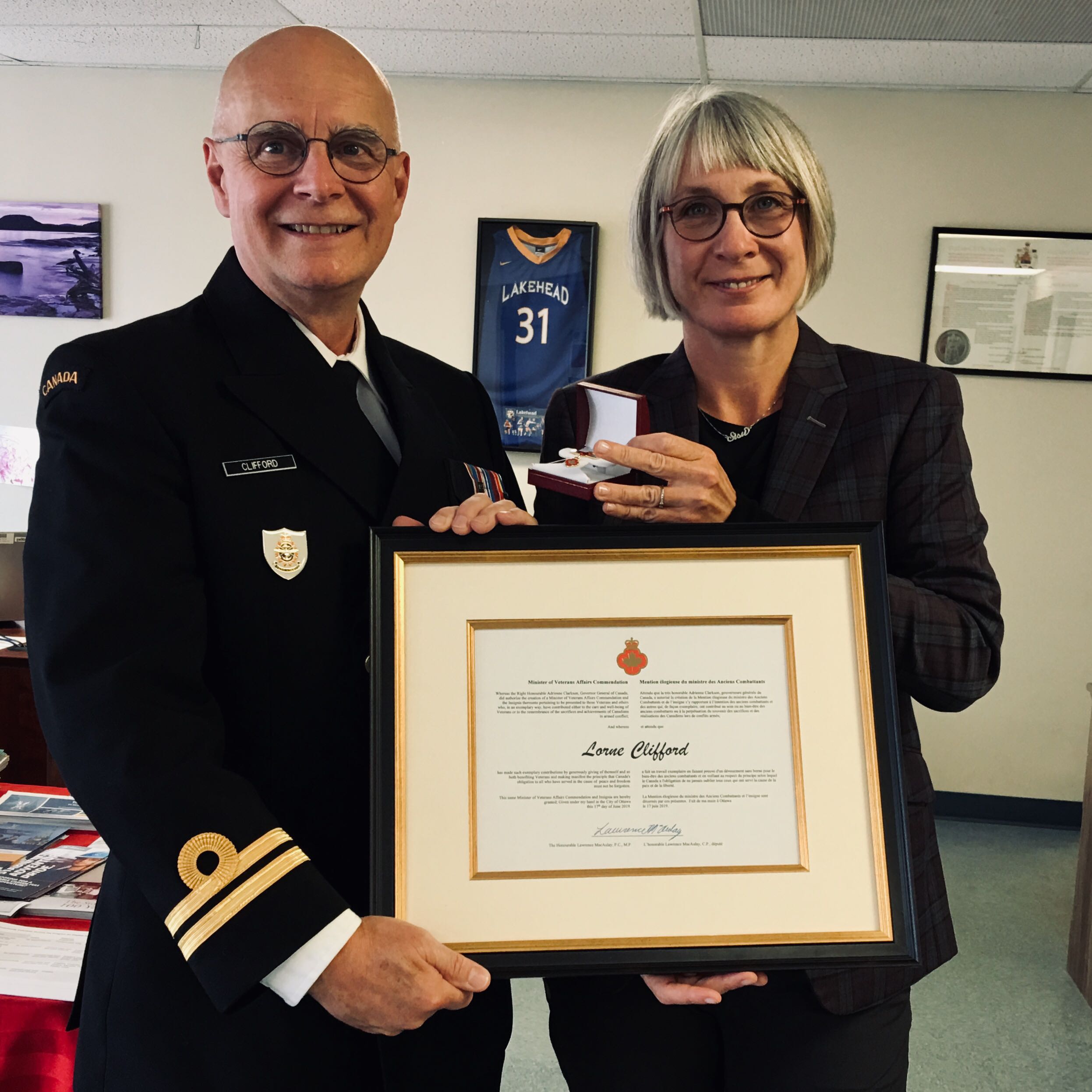 Lorne Clifford, wearing a military uniform, stands next to MP Patti Hajdu, while they display a framed Minister of Veterans Affairs Commendation for Lorne Clifford