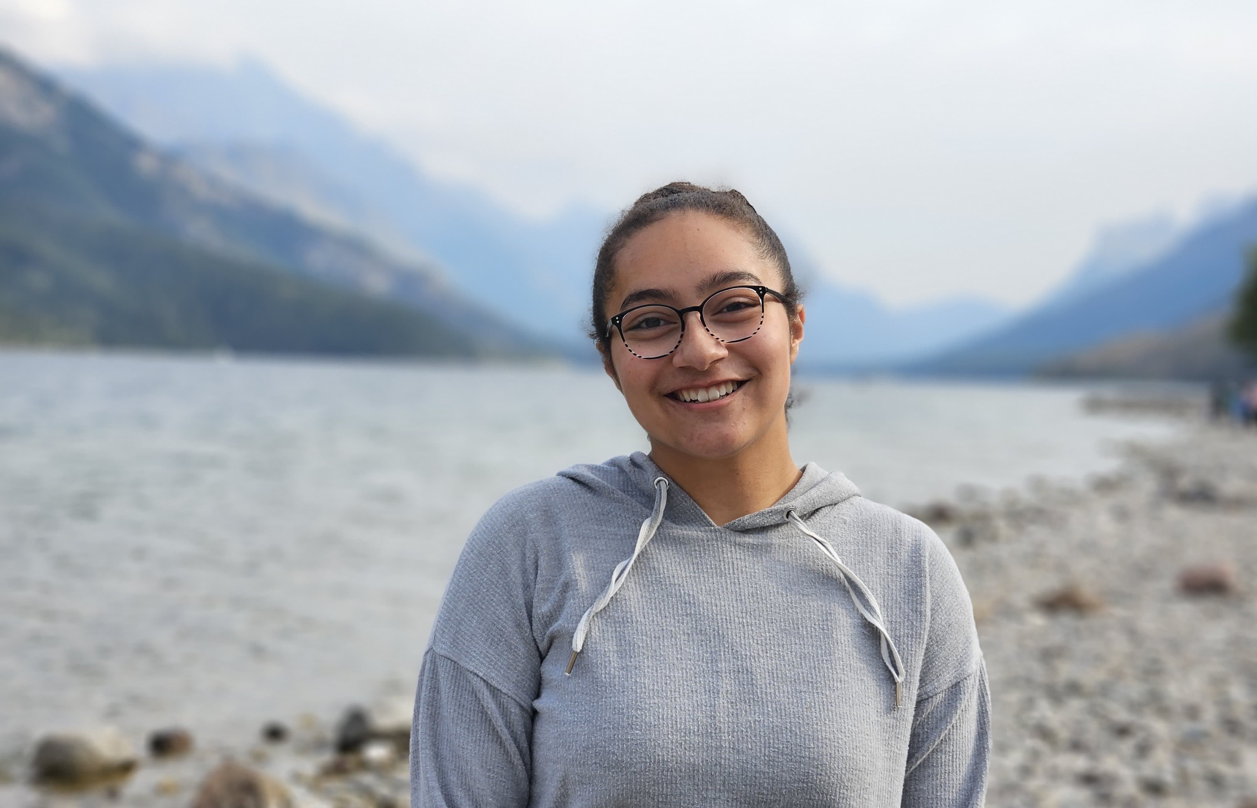 Mary Clark stands on the shores of a lake with mountains in the background