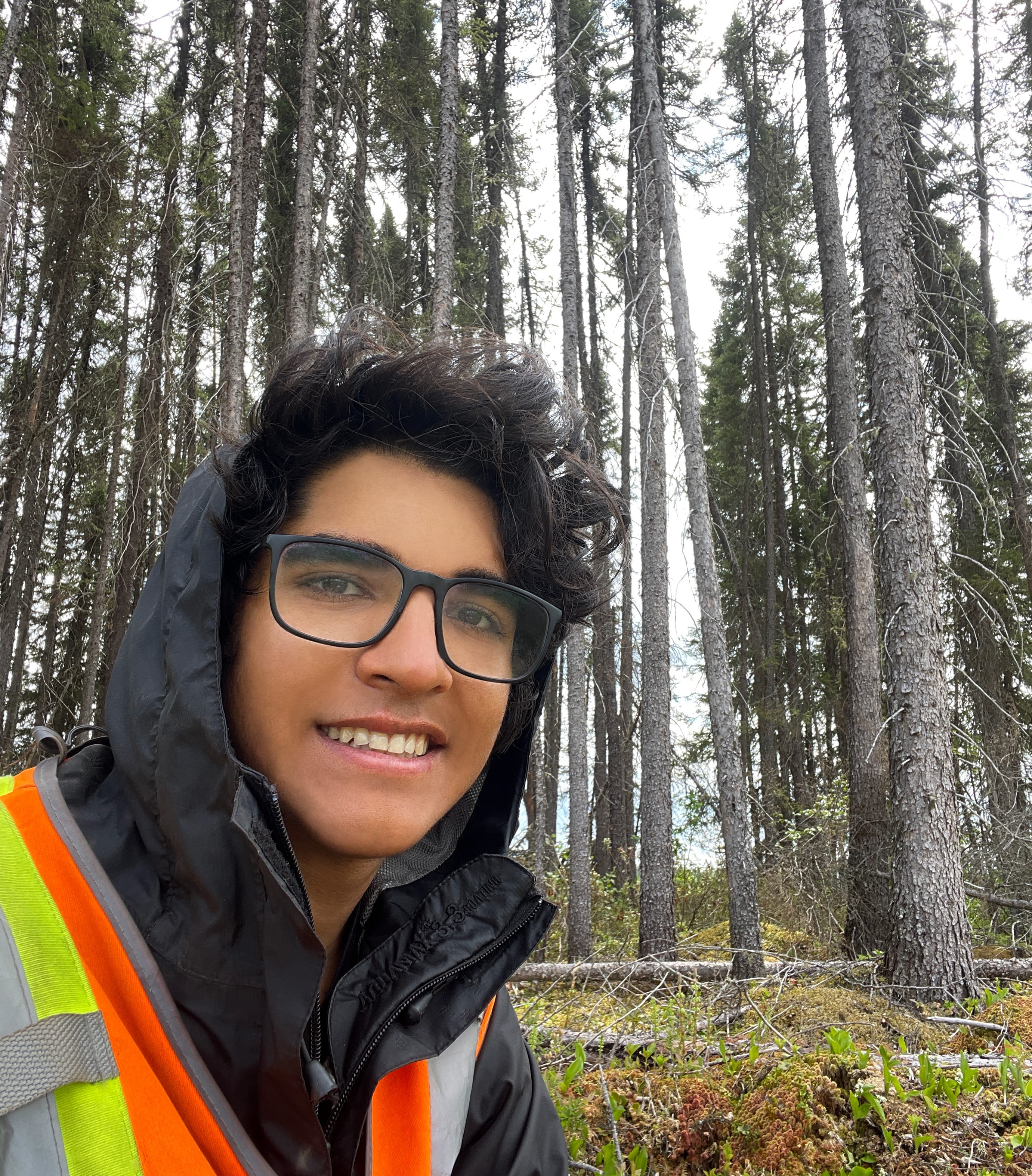 Mateo Velasco Alva in Forest Mateo Velasco Alva stands in coniferous forest wearing a black hooded jacket and an orange safety vest