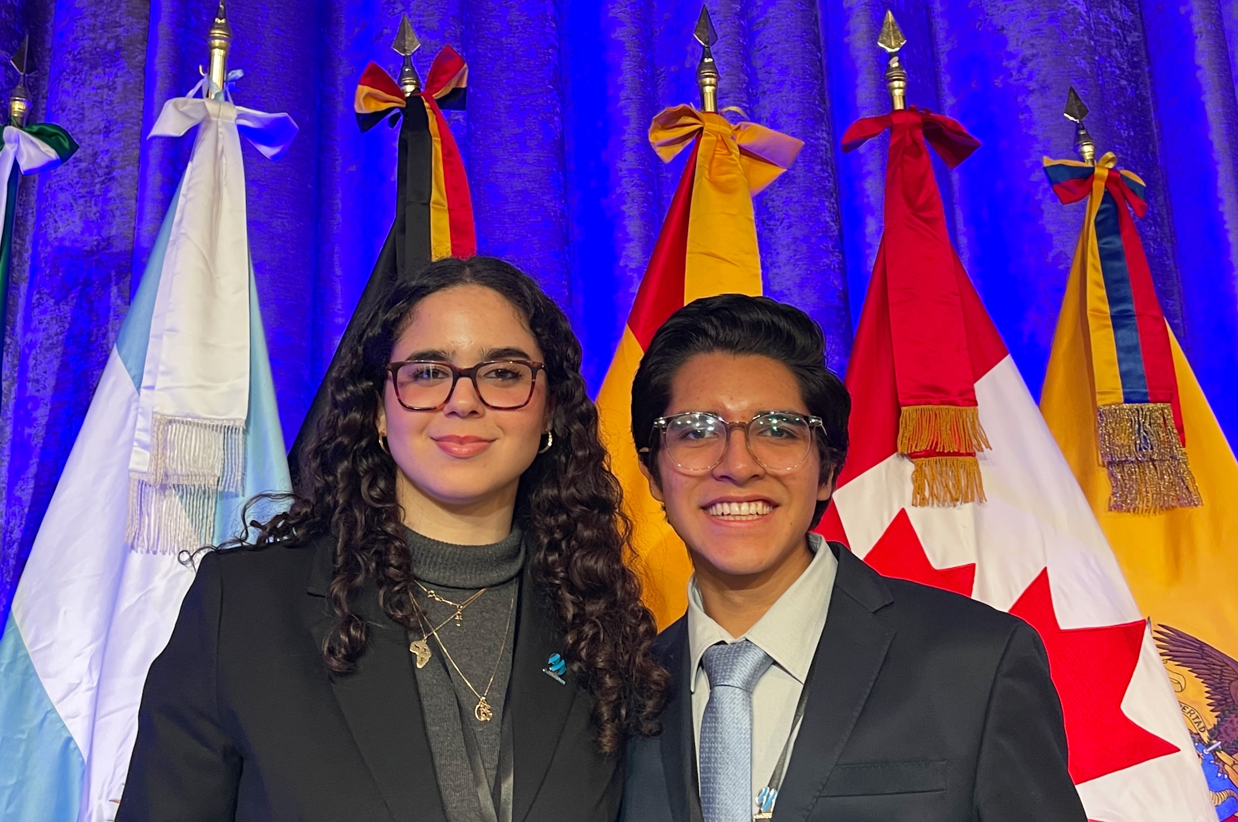 Inés Belkhodja & Mateo Velasco Alva Inés Belkhodja and Mateo Velasco Alva stand in front of a row of flags