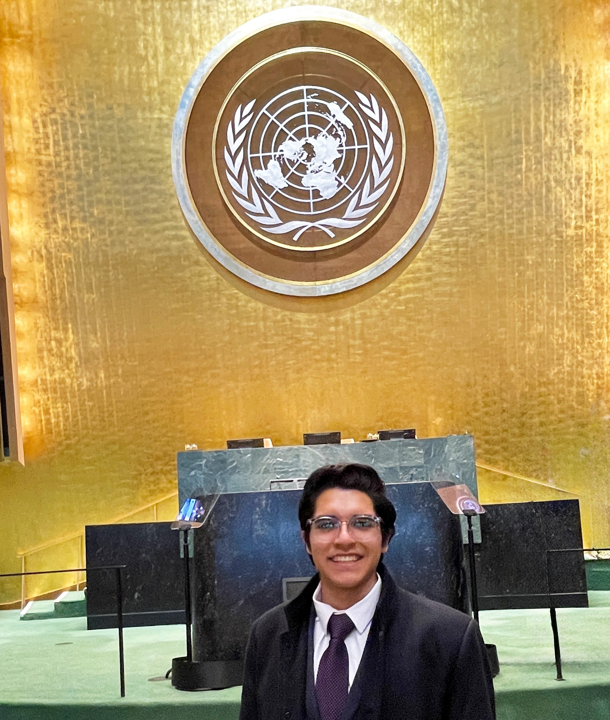 Mateo Velasco Alva in UN General Assembly Hall Mateo Velasco Alva Stands in the UN General Assembly Hall in front of a large marble desk; the United Nations logo hangs on the wall above the desk