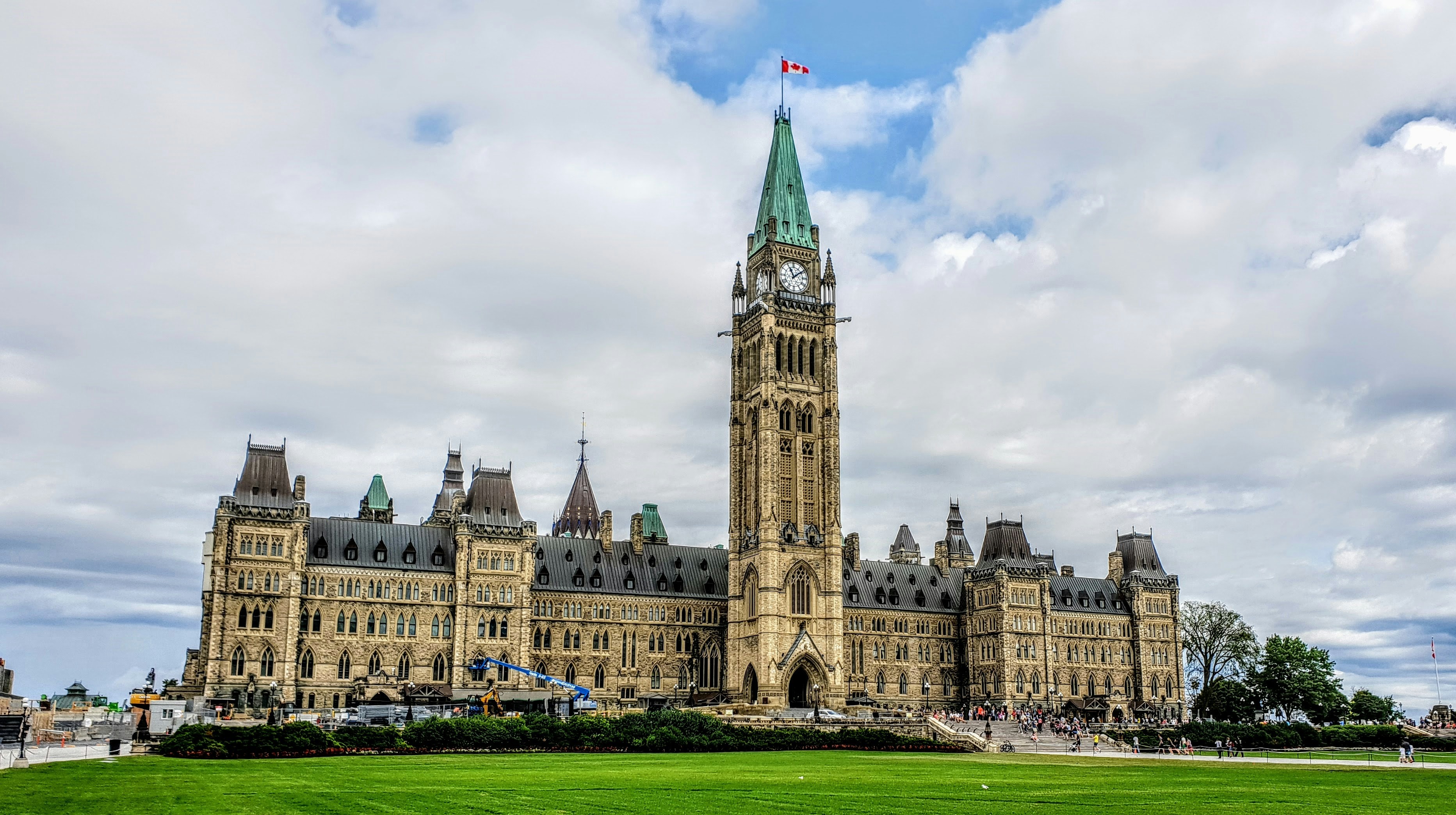 A view of Parliament Hill in Ottawa showing an ornate Gothic-style stone building with a central clock tower flying a Canadian flag