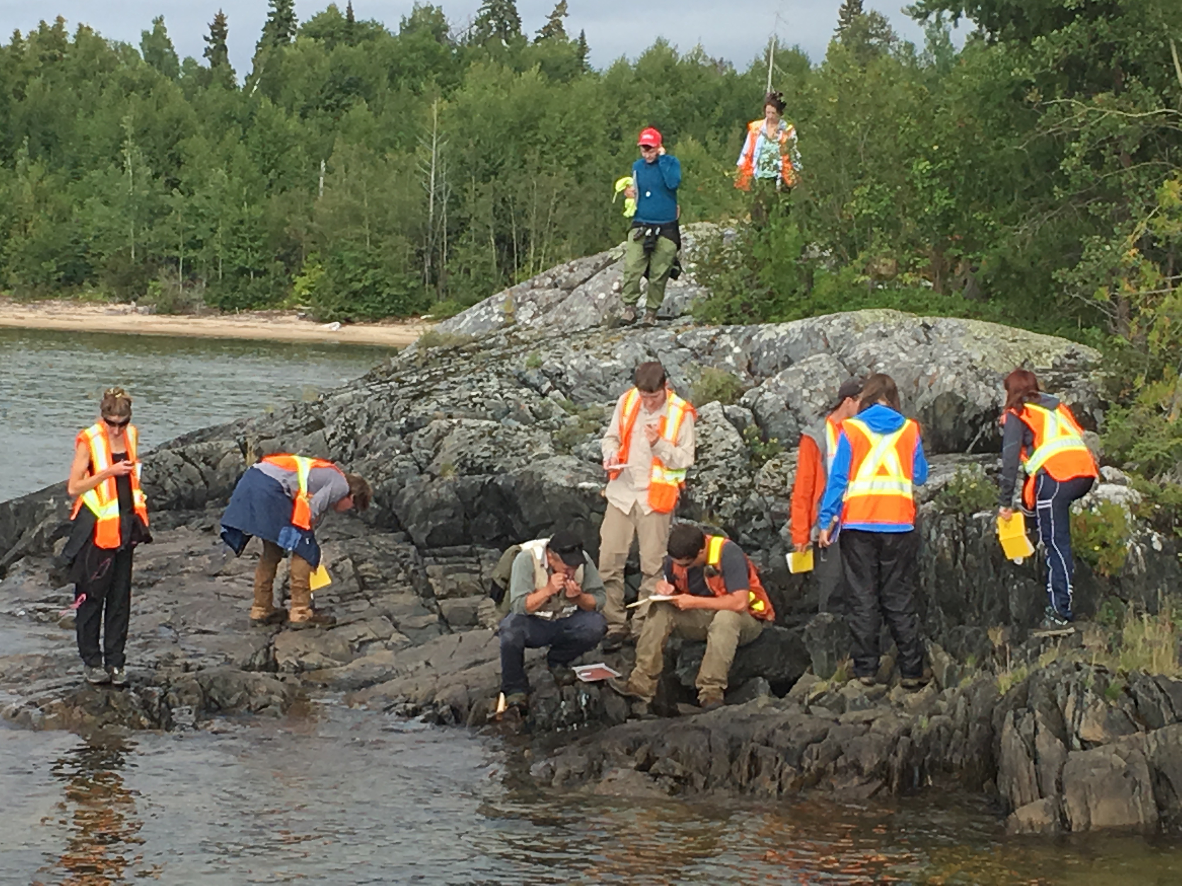Lakehead geology students in reflective vests on a rocky outcropping beside water body