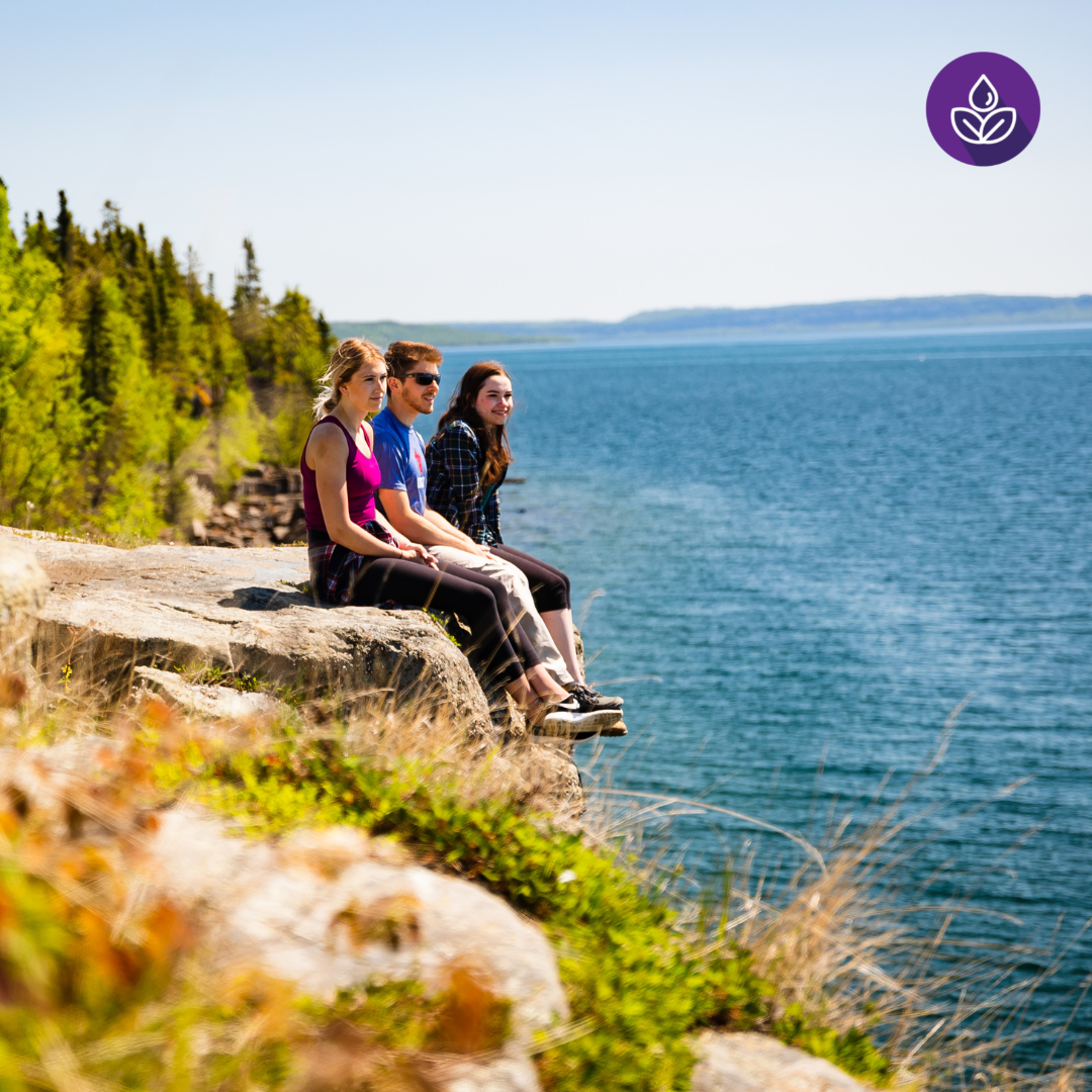 Three students sitting on a cliffside overlooking the water.