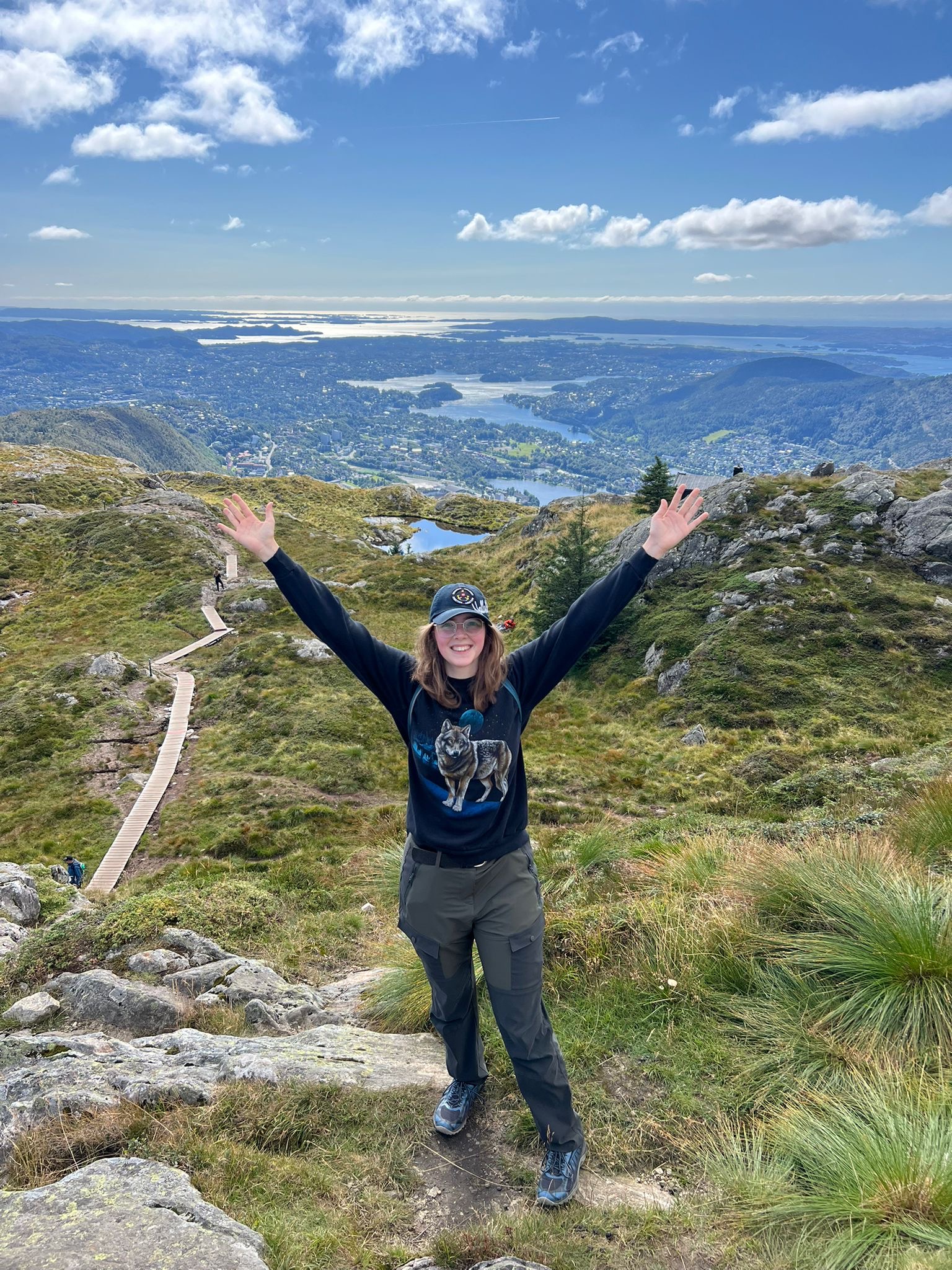 Student standing on mountain smiling with arms above head
