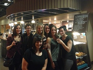 Seven people standing in front of the coffee bar in the Study enjoying some wine.