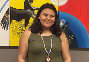 Nevaeh Matthews, achievement program student standing in front of Indigenous artwork